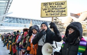Photo credit (clergy protesters): Religion News Service | Pictured: A line of clergy protesters. Pastor Joe Larson appears far right, wearing a black hood.